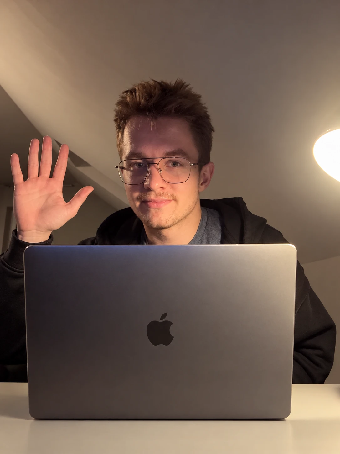 Cyprian Nowak macha na powitanie zza laptopa przy biurku